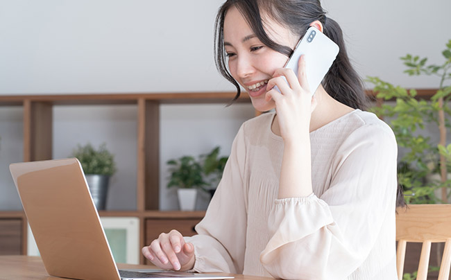 パソコンを見ながら電話をかけている女性